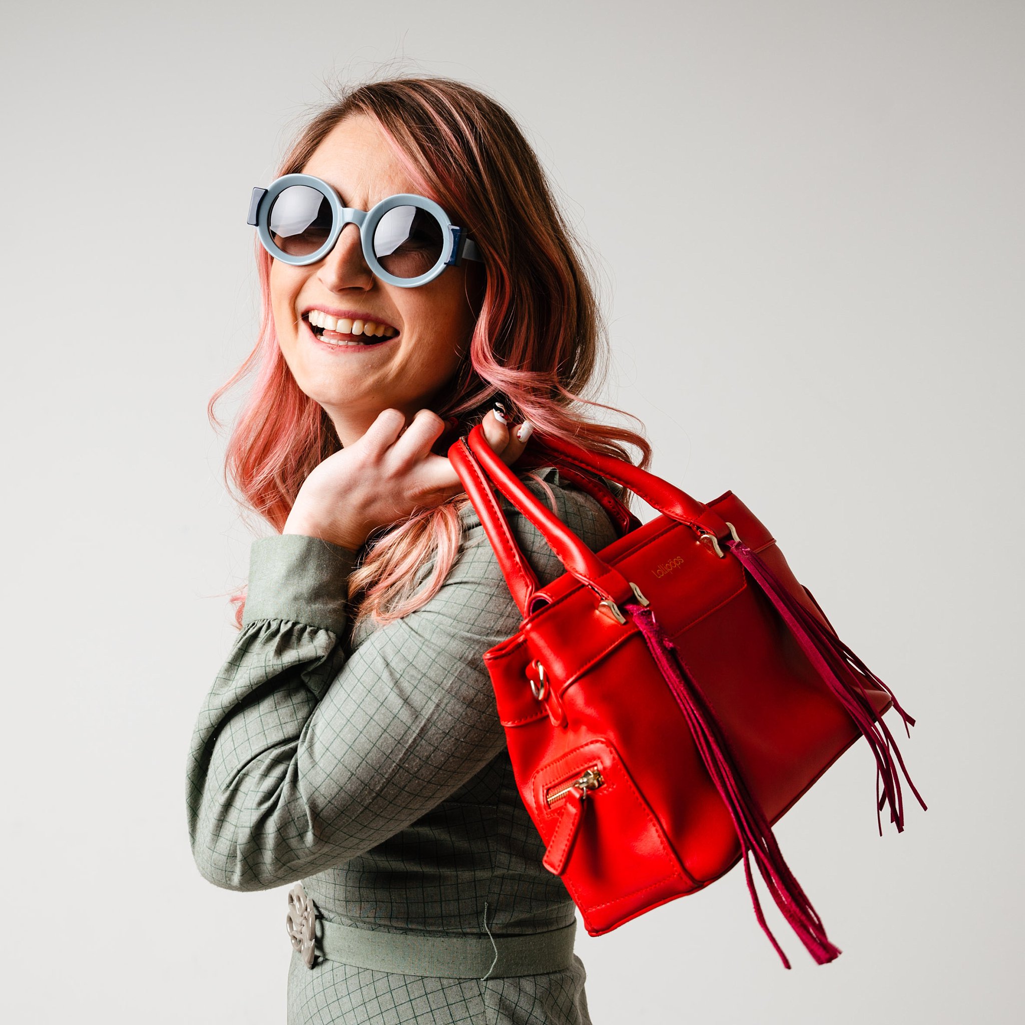 une femme pose face àl'appreile photo avec un sac rouge et des lunettes de soleil